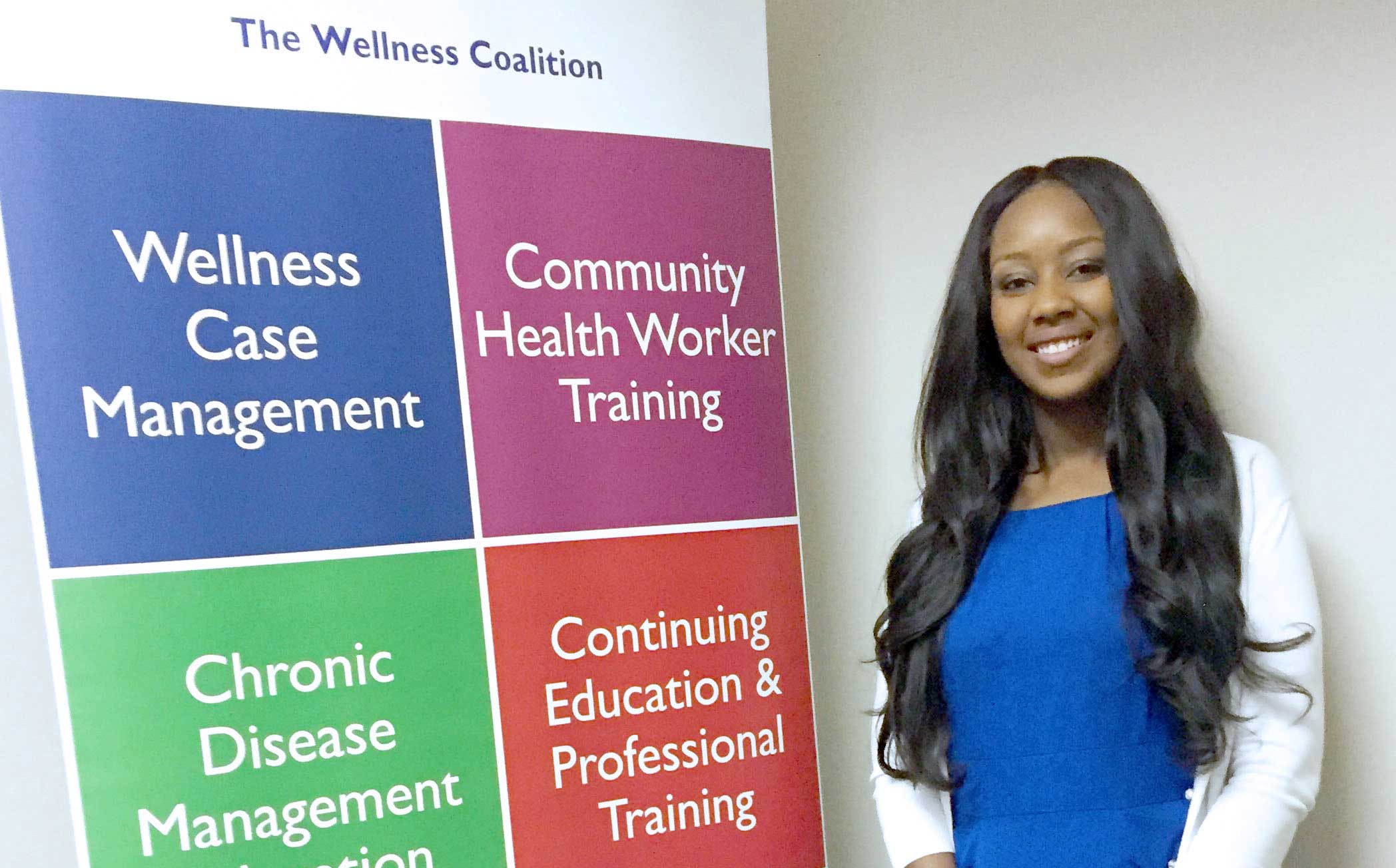 a woman posing woman standing next to a colorful posterboard for wellness coalition
