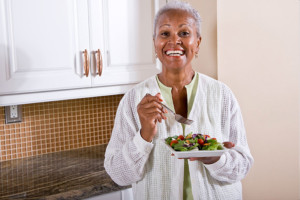 Older woman eating a plate of vegetables and smiling.