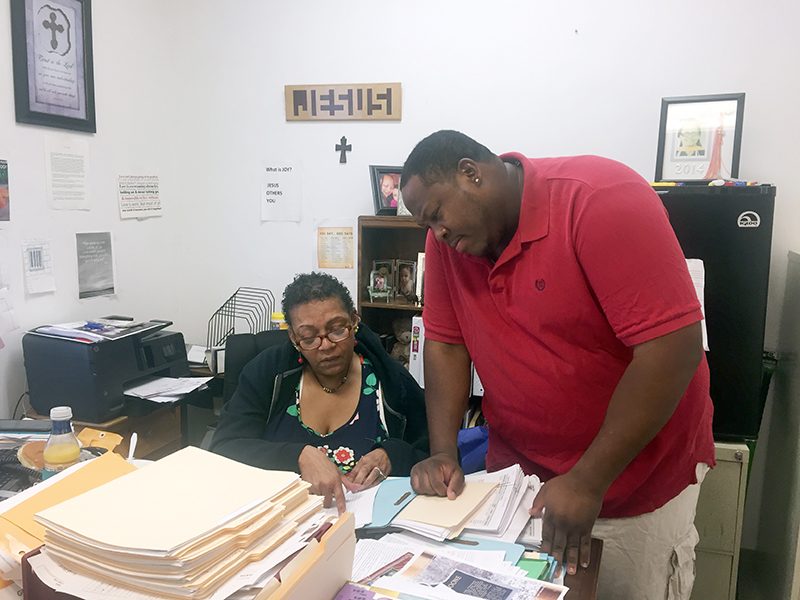 Sophia-Dowdell,-Case-Manager-at-Friendship-Mission-West,-with-shelter-resident-Kei-Johnson-for-web Case manager, Sophia Dowdell, showing a man something in a file at a desk.